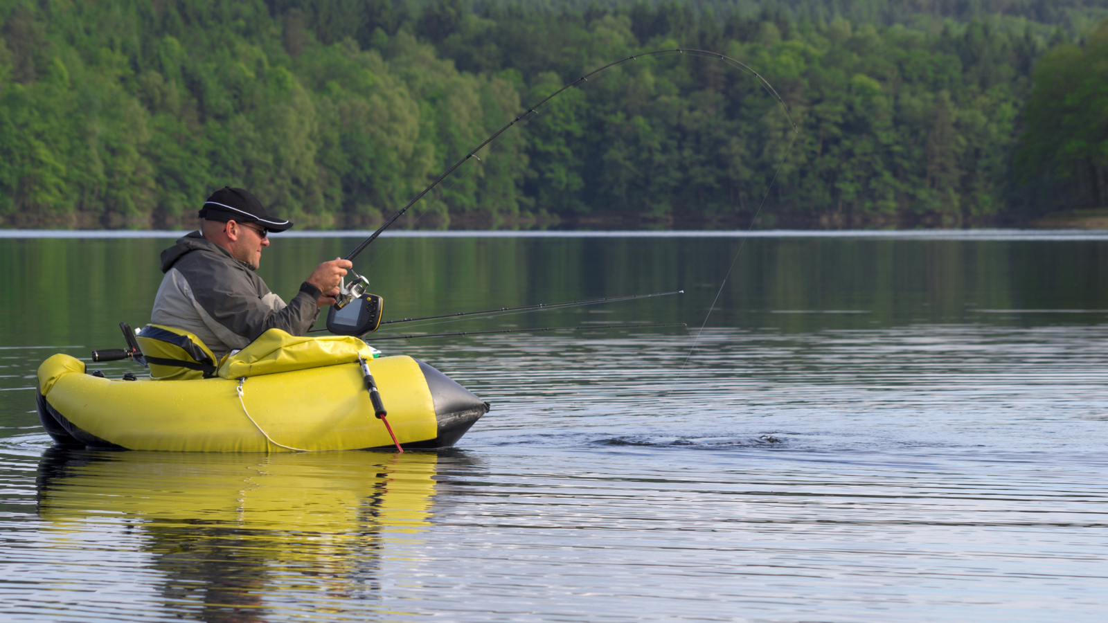 Pêcheur assis sur un float tube jaune, sur un lac, vu de profil